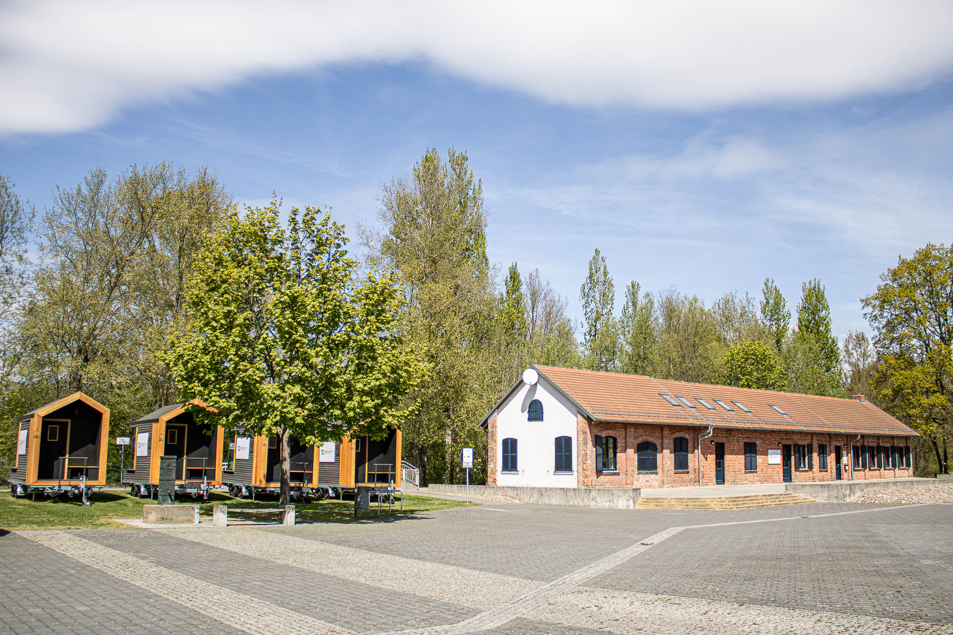 Foto des Incubator Village Beeskow mit auf der linken Seite vier Tiny Spaces und auf der rechten Seite das Backsteingebäude der alten Tischlerei
